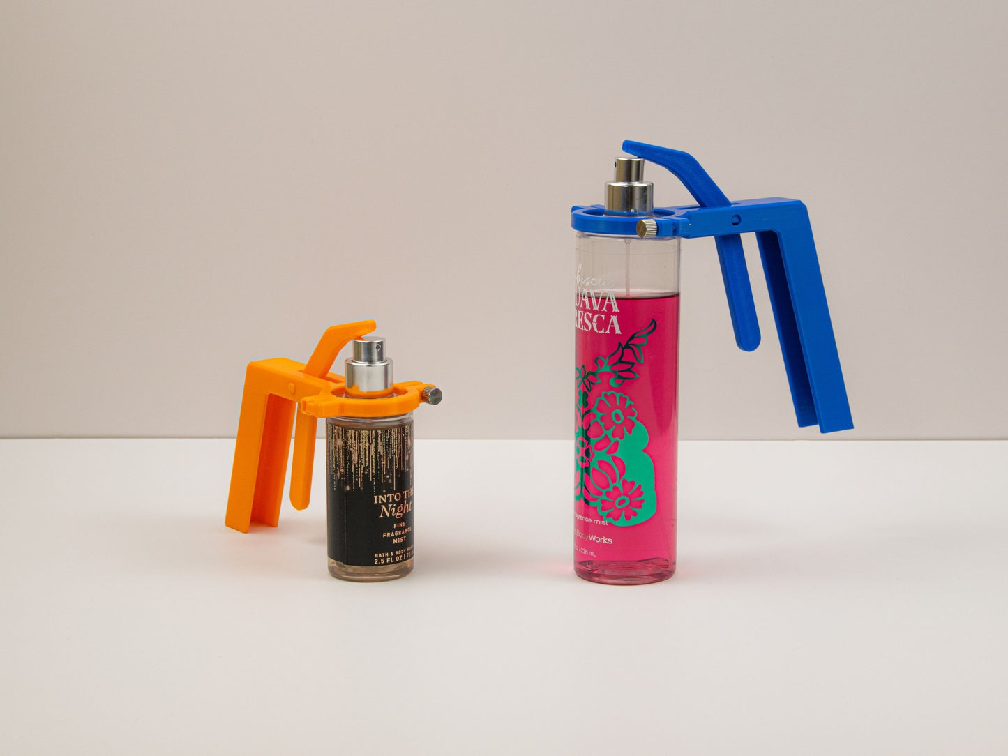 Simple photo showing the two sizes of the body spray assistant—small (orange) and large (blue)—each attached to a different Bath & Body Works spray bottle.