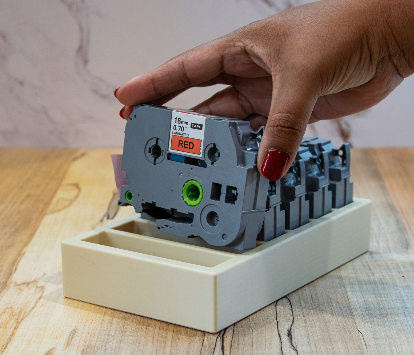 Hand placing an 18mm laminated red label tape into a beige organizer tray designed for Brother P-Touch cartridges.