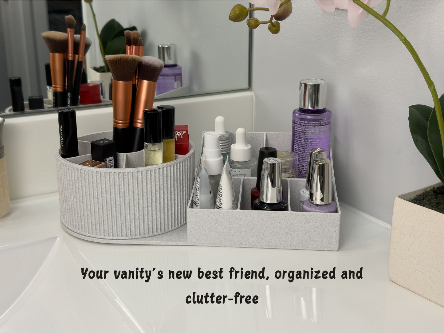 Rotating beauty organizer on a white vanity: round carousel with six pie-shaped slots and a center well beside a five-compartment base, neatly holding brushes, nail polish, and serums; orchid and mirror in background; on-image caption reads ‘Your vanity’s new best friend, organized and clutter-free.’