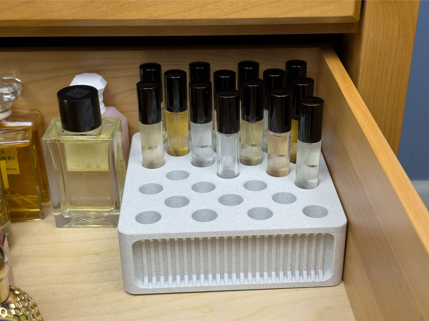 Square ScentSplit perfume organizer placed neatly in a wooden drawer alongside full-size perfume bottles. The perfume organizer holds multiple ScentSplit decants upright, maximizing space efficiency while keeping the vials accessible. The recessed ribbing design on the front face is clearly visible against the light wood drawer interior.