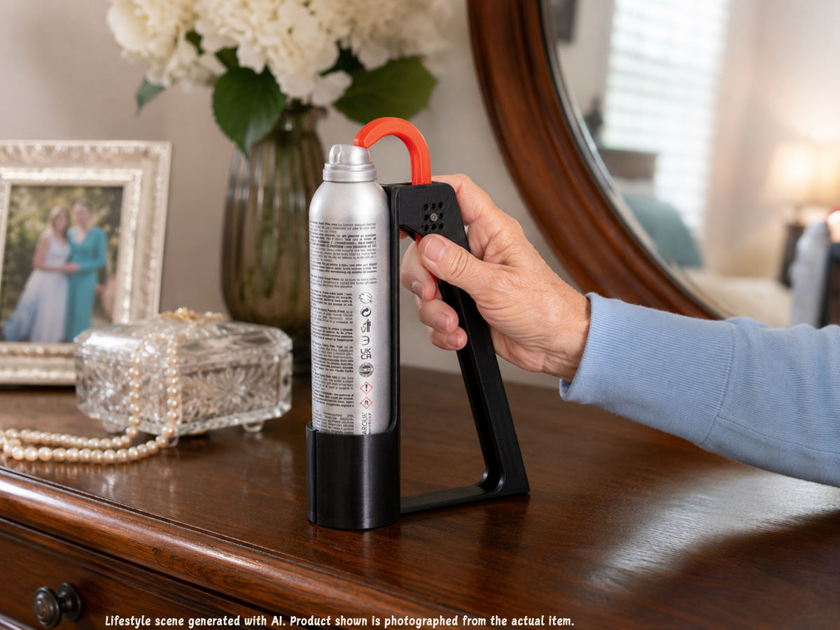 Older adult’s hand using the Hairspray Assistant on a dresser beside jewelry, a framed photograph, and a mirror.