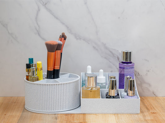 Rotating beauty organizer on a wood surface with a light stone-look backdrop: the rotating round carousel on the left and the rectangular five-compartment base on the right, both in a light speckled gray finish.