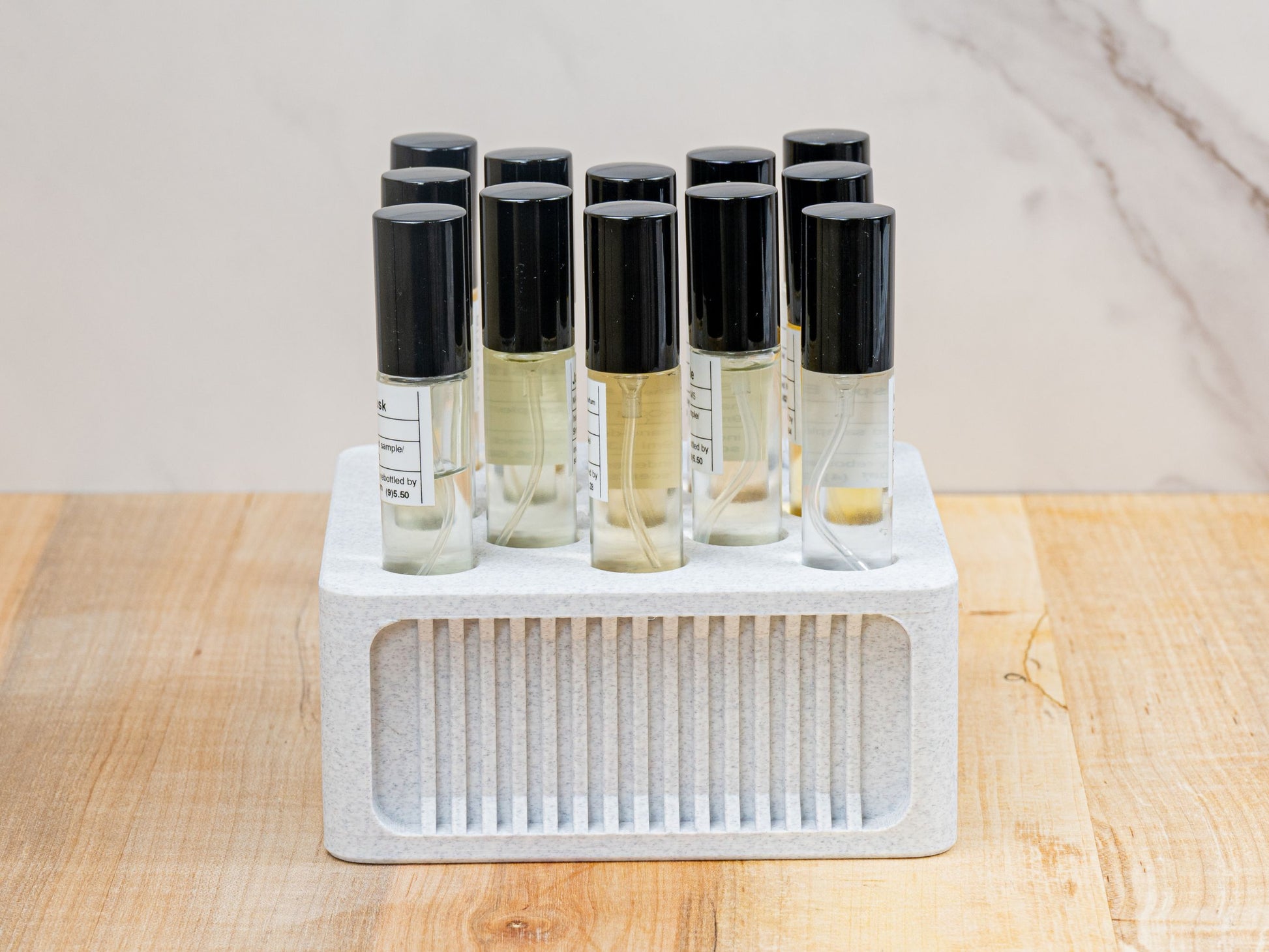 Straight-on product shot of the square ScentSplit perfume organizer, filled with multiple ScentSplit decants. The perfume organizer sits on a wood surface with a light marble backdrop. Its clean geometry, recessed ribbing, and uniform arrangement of vials highlight its balance of functionality and display-worthy style.