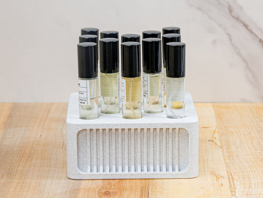Straight-on product shot of the square ScentSplit perfume organizer, filled with multiple ScentSplit decants. The perfume organizer sits on a wood surface with a light marble backdrop. Its clean geometry, recessed ribbing, and uniform arrangement of vials highlight its balance of functionality and display-worthy style.
