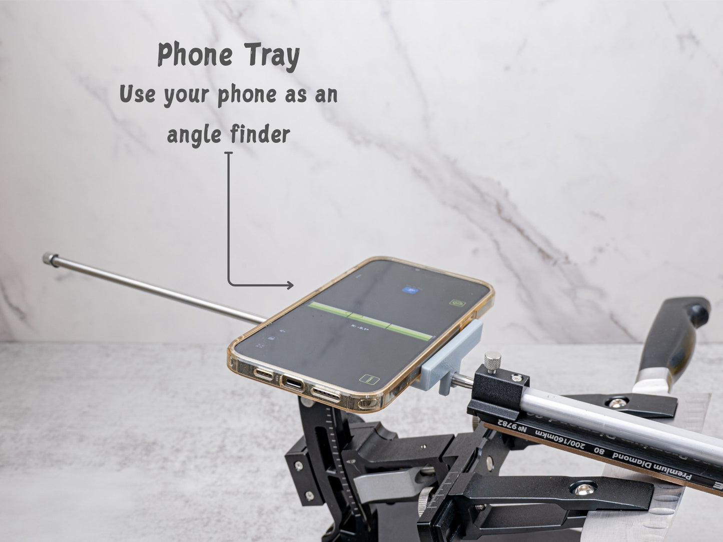 Phone tray mounted on the XARILK Gen 3 knife sharpener holding a smartphone horizontally, showing a digital level app being used as an angle finder while sharpening a knife.
