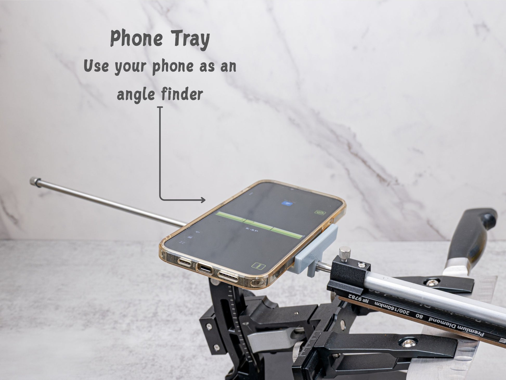 Phone tray mounted on the XARILK Gen 3 knife sharpener holding a smartphone horizontally, showing a digital level app being used as an angle finder while sharpening a knife.