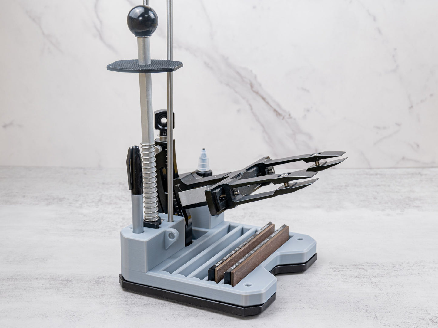 Xarilk Gen 3 Knife Sharpener with organizer tray installed, showing sharpening stones stored in the tray, guide rods mounted, and a knife secured in the clamp for sharpening.